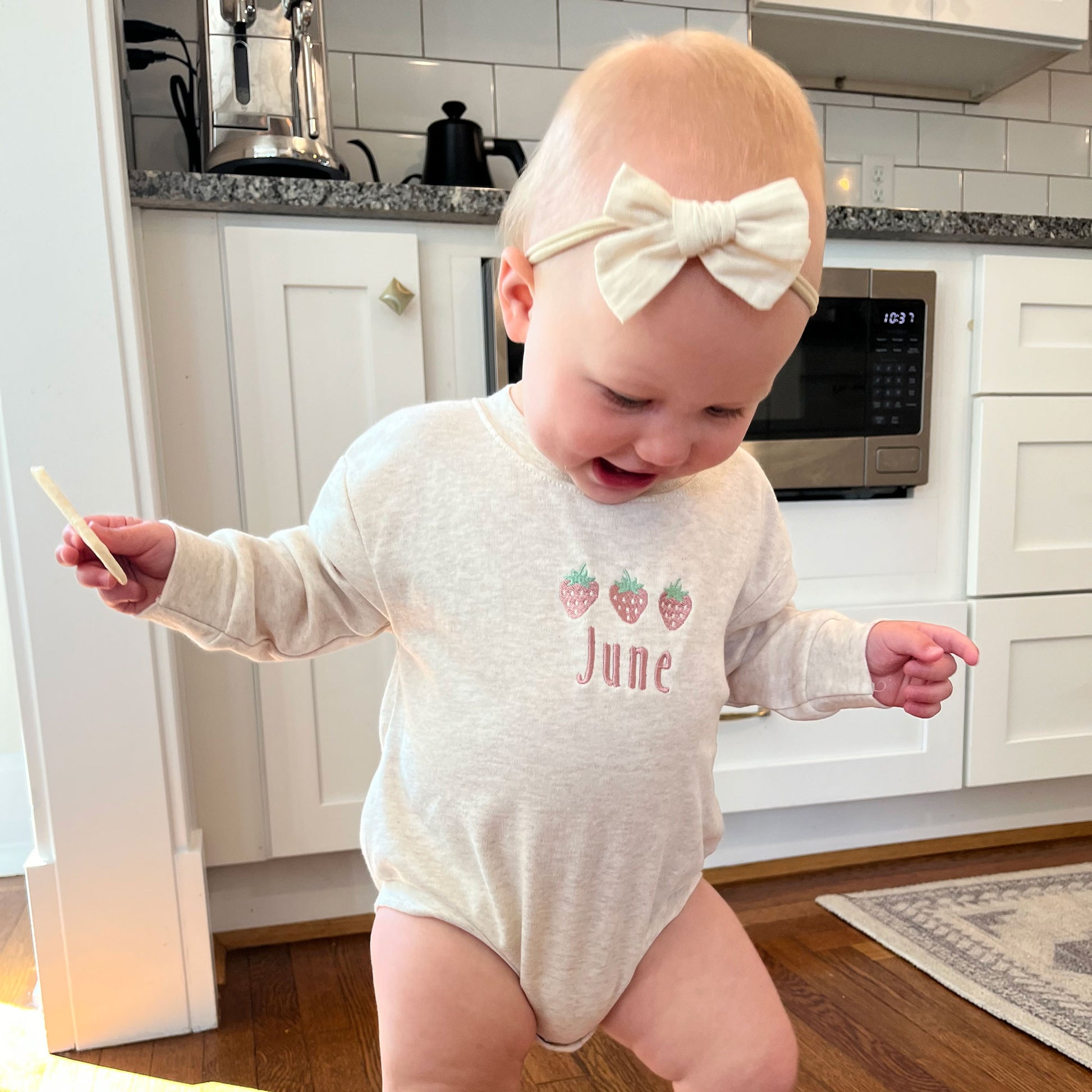 baby girl wearing an oat bubble romper with custom strawberry and name embroidered design