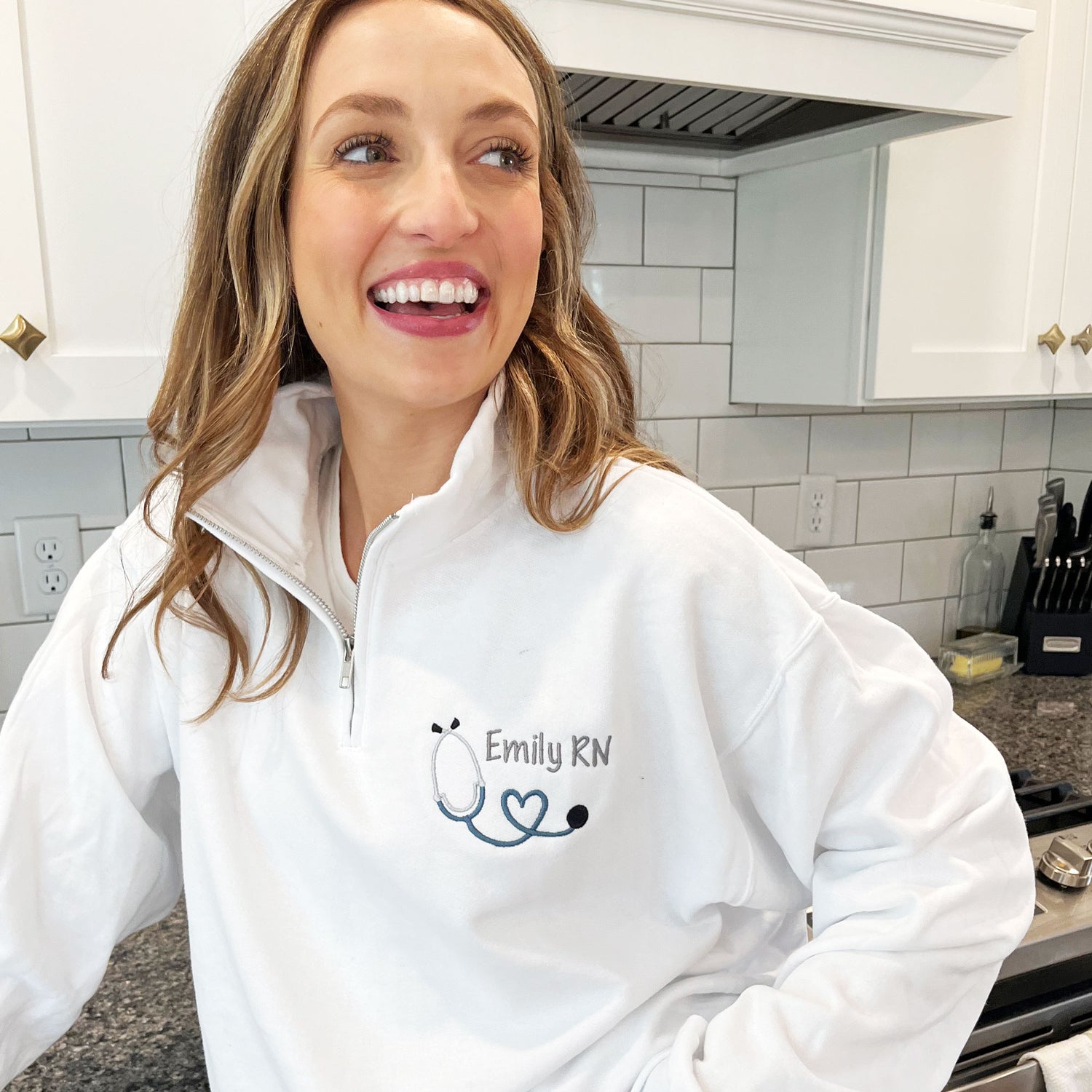 woman wearing a white quarter zip with custom heart stethoscope and name embroidered design on the left chest
