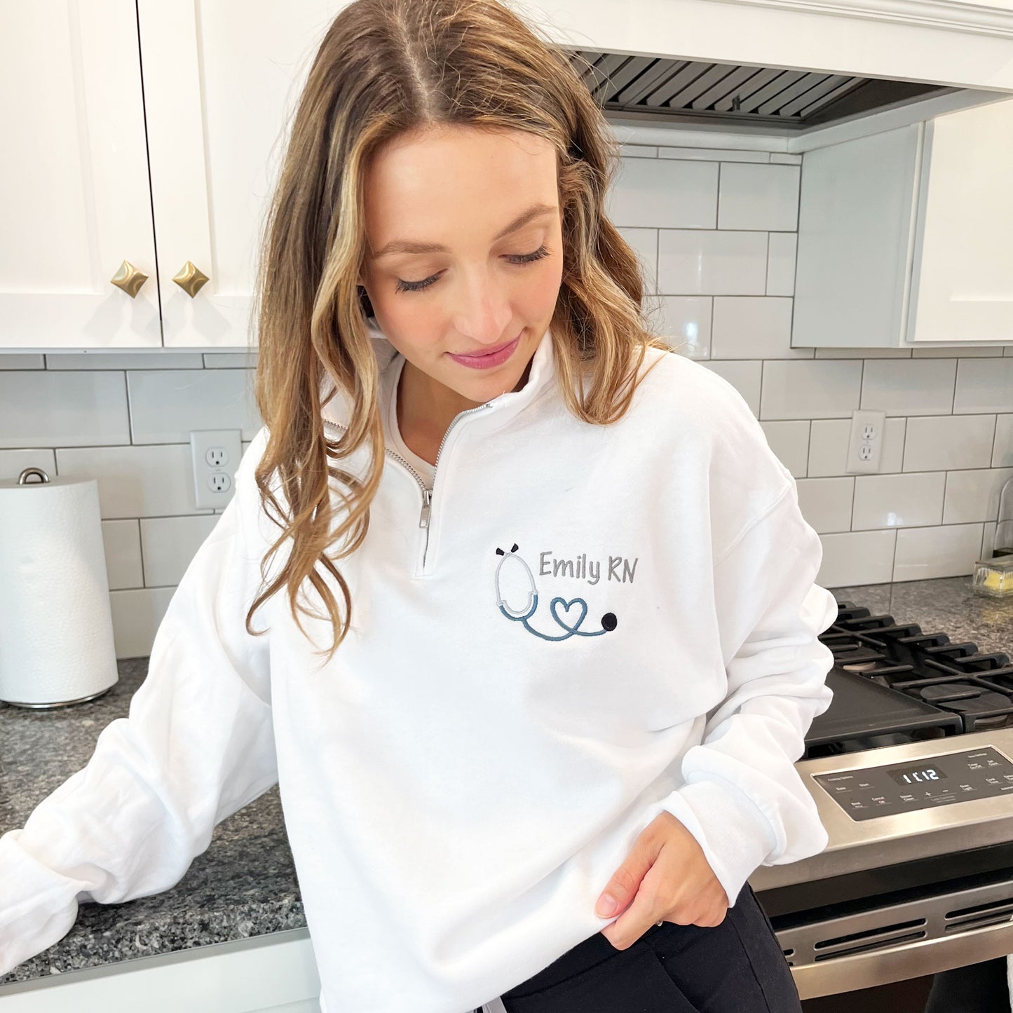 women modeling a white quarter zip pullover sweatshirt with a custom name and mini heart stethoscope embroidered design on the left chest.