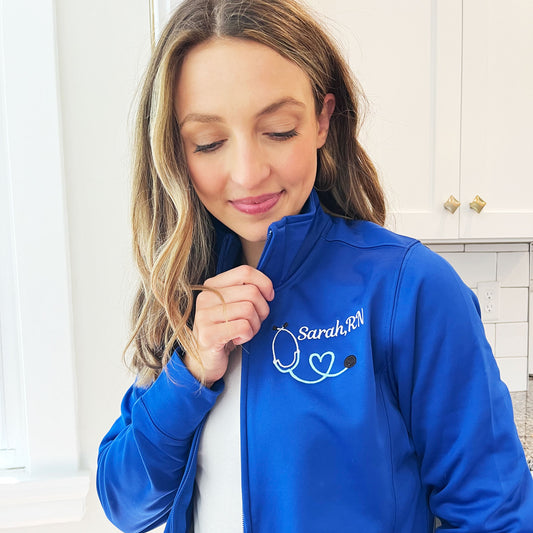 woman wearing a royal blue full zip polyester jacket with embroidered nurse stethoscope and custom name design