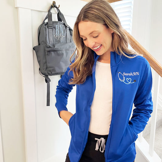woman wearing a royal blue full zip polyester jacket with embroidered nurse stethoscope and custom name design on the left chest