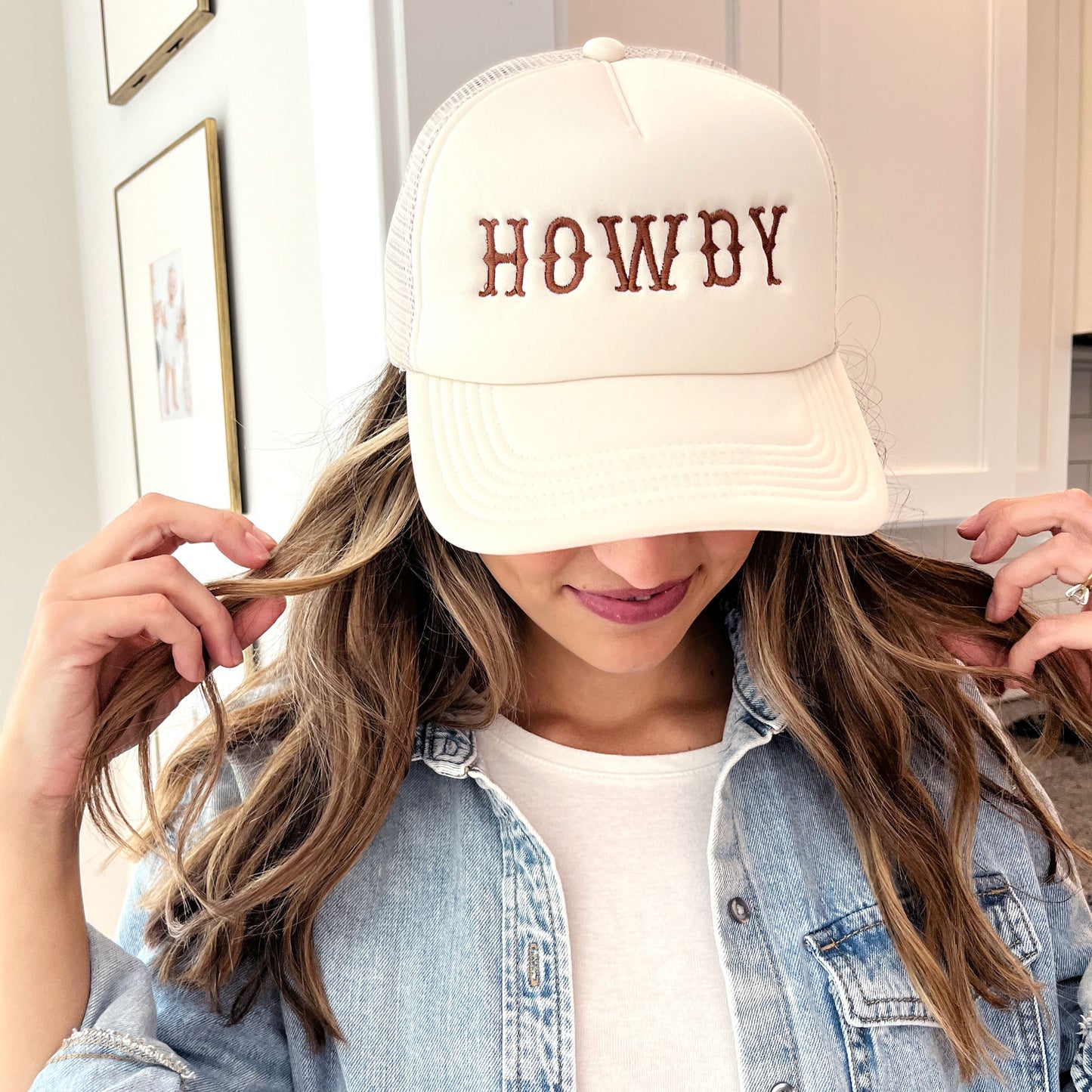 woman wearing a sand trucker hat with embroidered all caps howdy design in brown thread