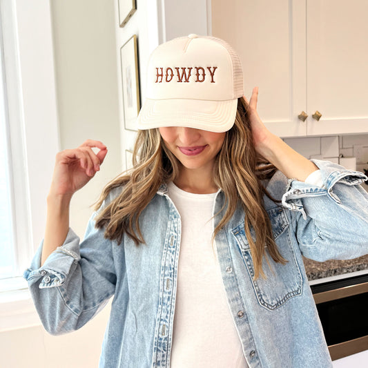woman wearing a sand trucker hat with embroidered all caps howdy design in brown thread