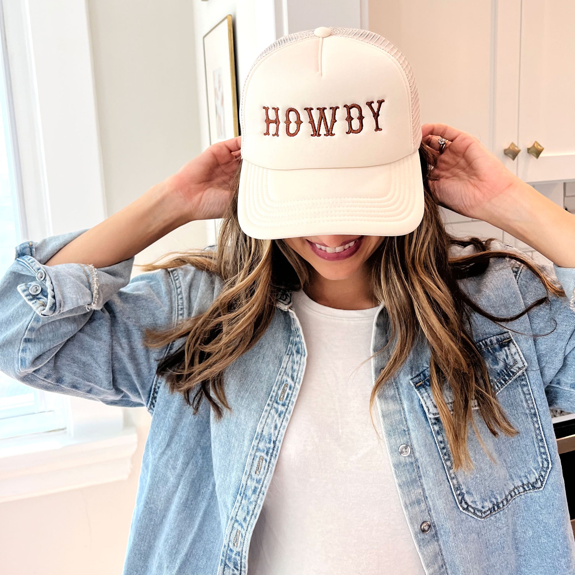 woman wearing a sand trucker hat with embroidered all caps howdy design in brown thread