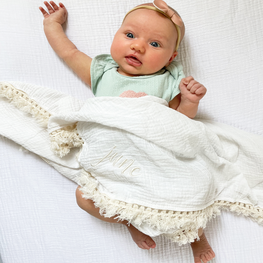 baby covered by a muslin baby blanket with decorative trim and custom embroidered name design on the corner