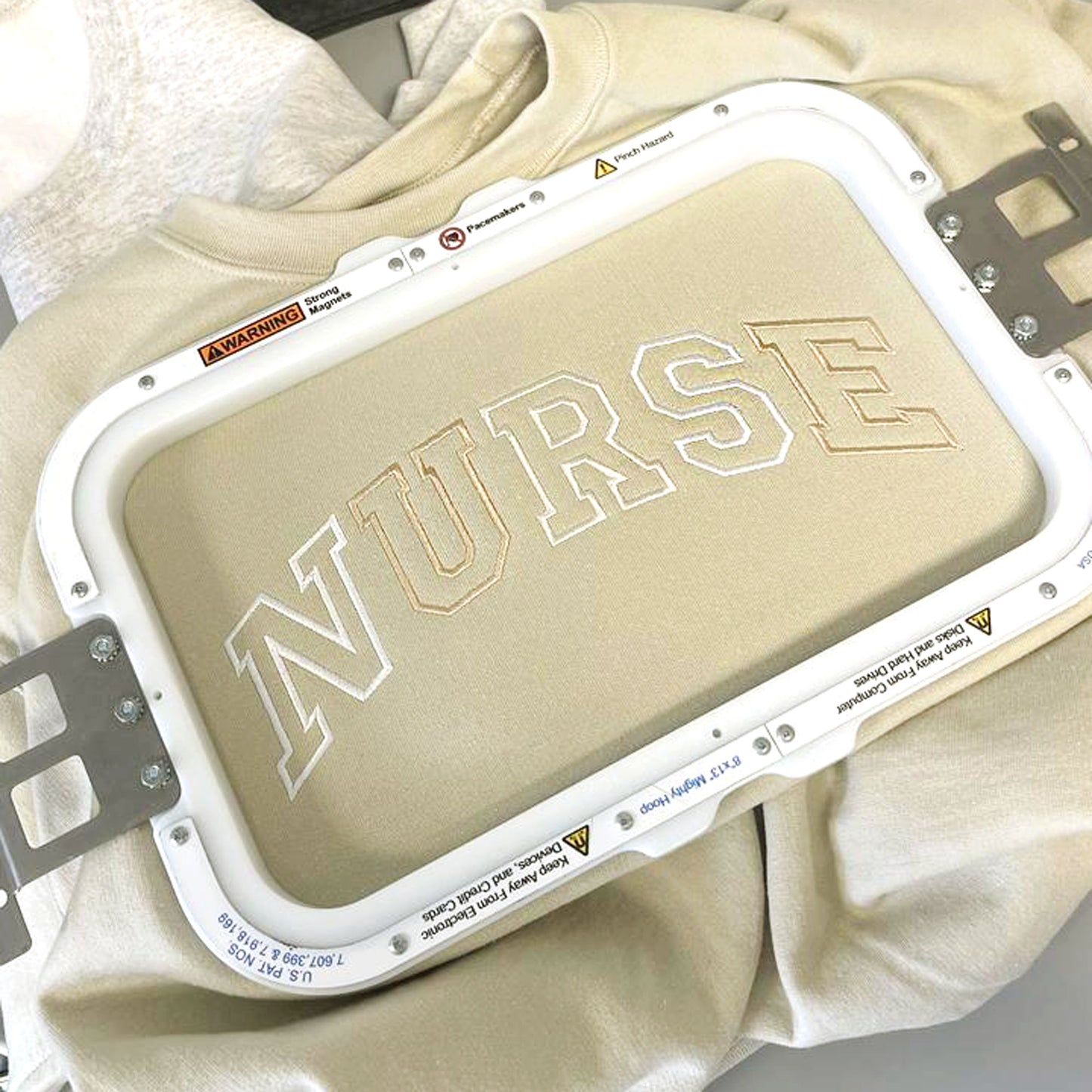 beige crewneck sweatshirt in embroidery hoop with NURSE embroidered in a varsity font across the chest