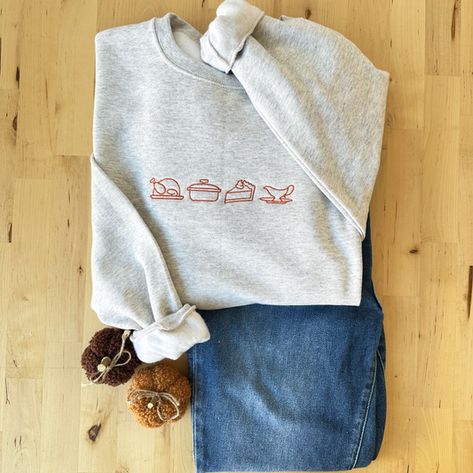 crewneck sweatshirt featuring an outlined turkey, casserole dish, pumpkin pie, and gravy boat outlined embroidered design