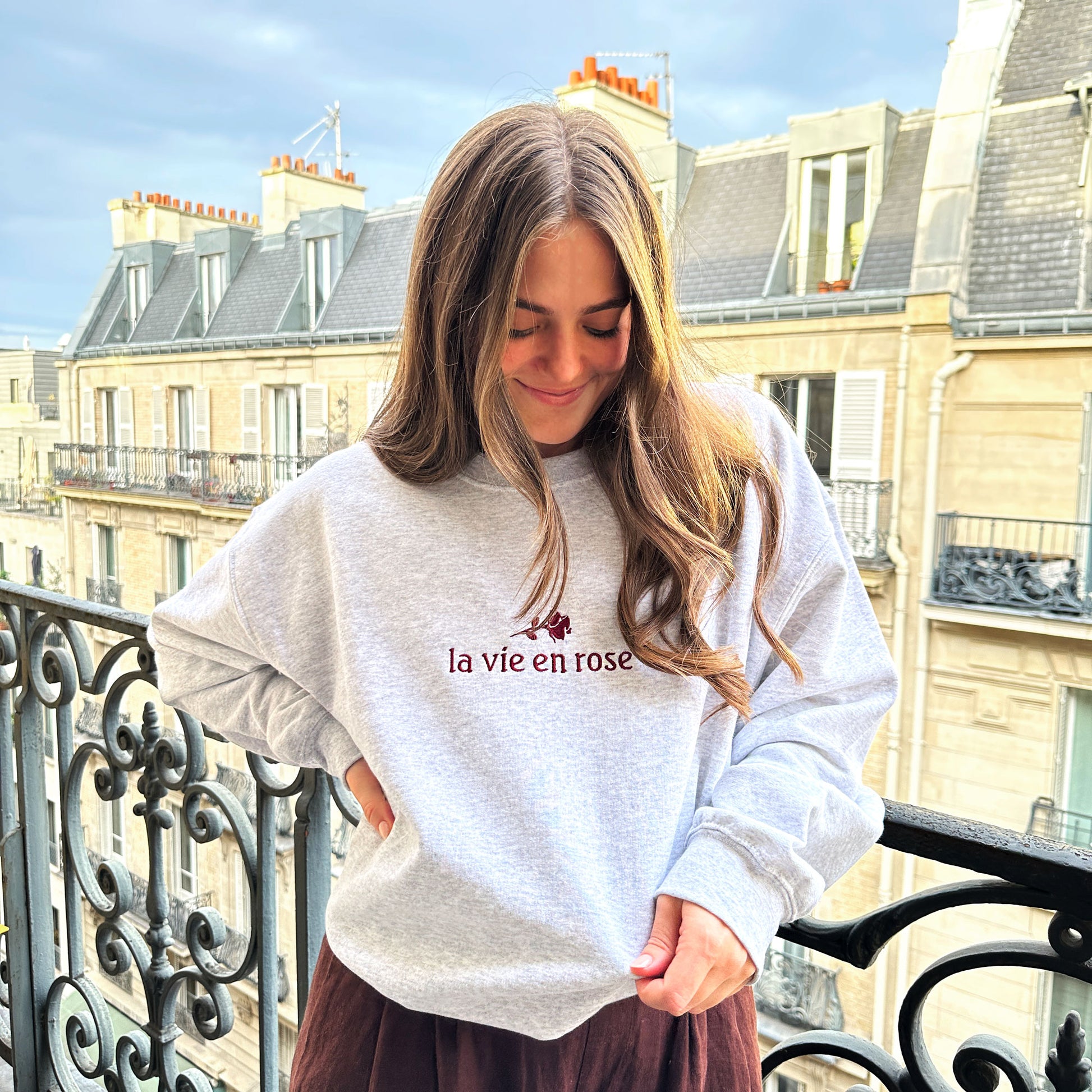 Woman wearing ash crewneck sweatshirt that has la vie en rose embroidered design