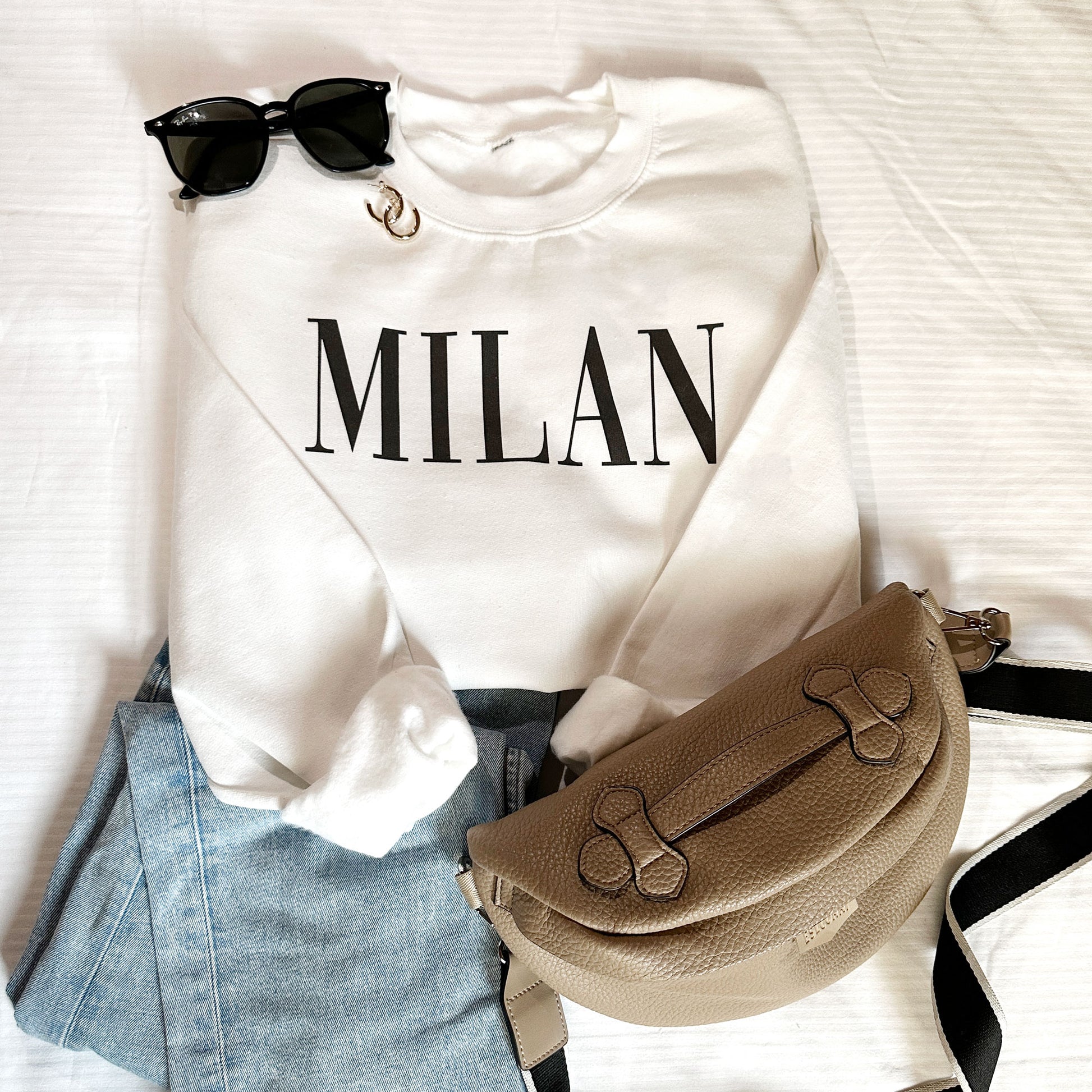 styled flat lay of a white crewneck sweatshirt with MILAN printed across the chest