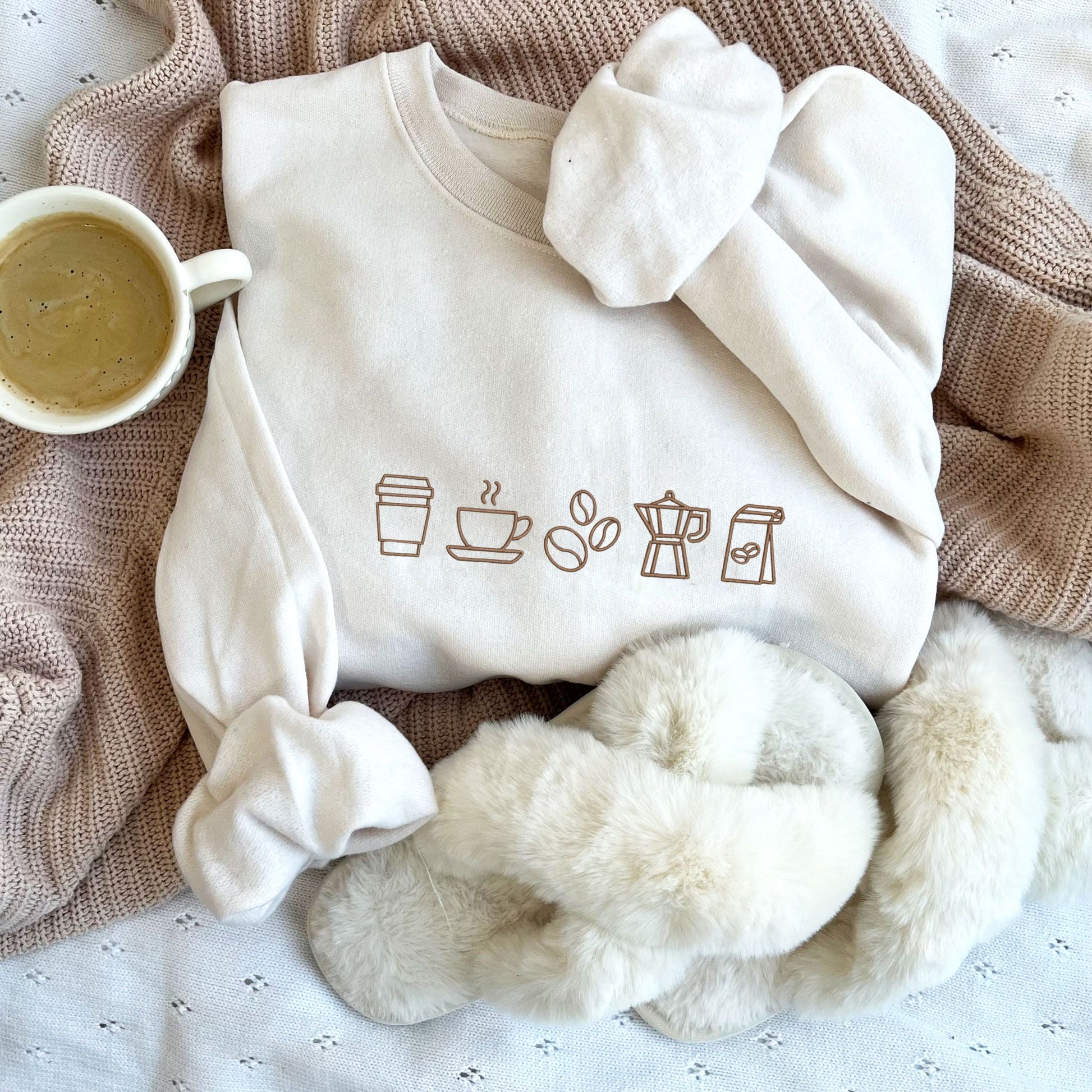 styled flat lay of a sweet cream green crewneck sweatshirt with embroidered coffee icons across the chest in chestnut  thread