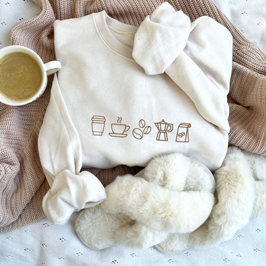 styled flat lay of a sweet cream green crewneck sweatshirt with embroidered coffee icons across the chest in chestnut  thread