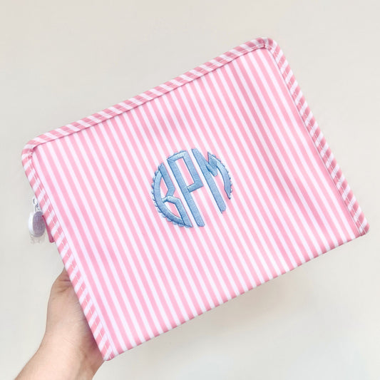 Pink and white striped pouch with blue monogram initials held by a hand on a light background