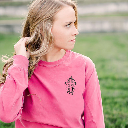 woman wearing a crunchberry comfort colors long sleeve shirt with a black flora embroidered cross on the left chest