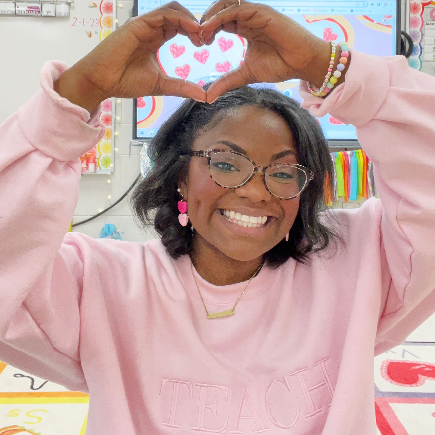young woman wearing a light pink crewneck sweatshirt with embroidered all caps teach in baby pink tone on tone thread