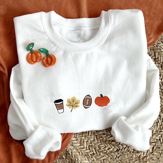 styled flat lay photo of a white crewneck sweatshirt with embroidered coffee, leaf, football, and pumpkin design across the chest.