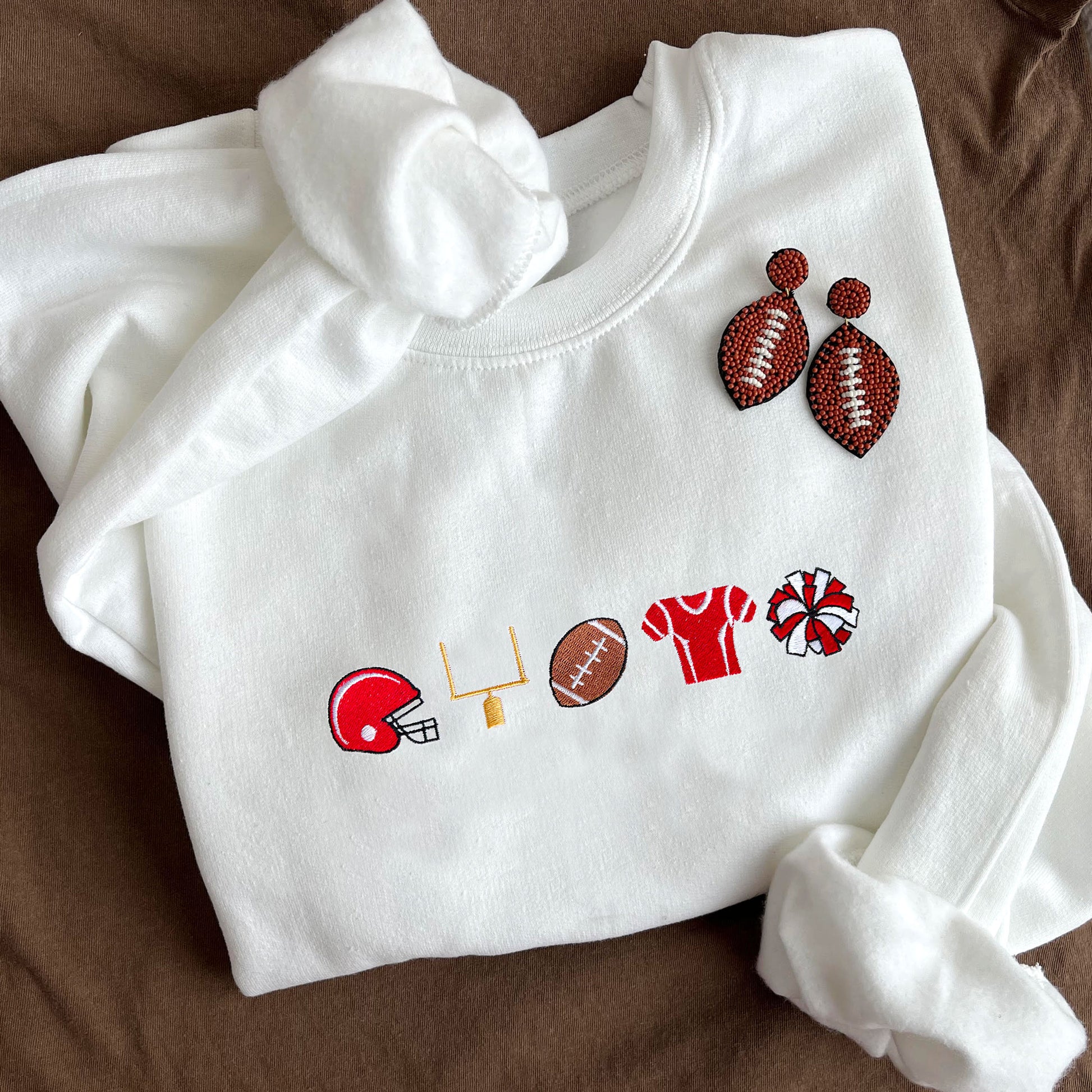 flat lay of a white crewneck sweatshirt with embroidered football icons across the chest with red accent color