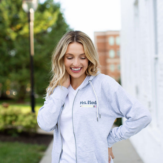 Blonde woman wearing athletic heather full zip jacket with double strings teacher name and pencil embroidered on left side
