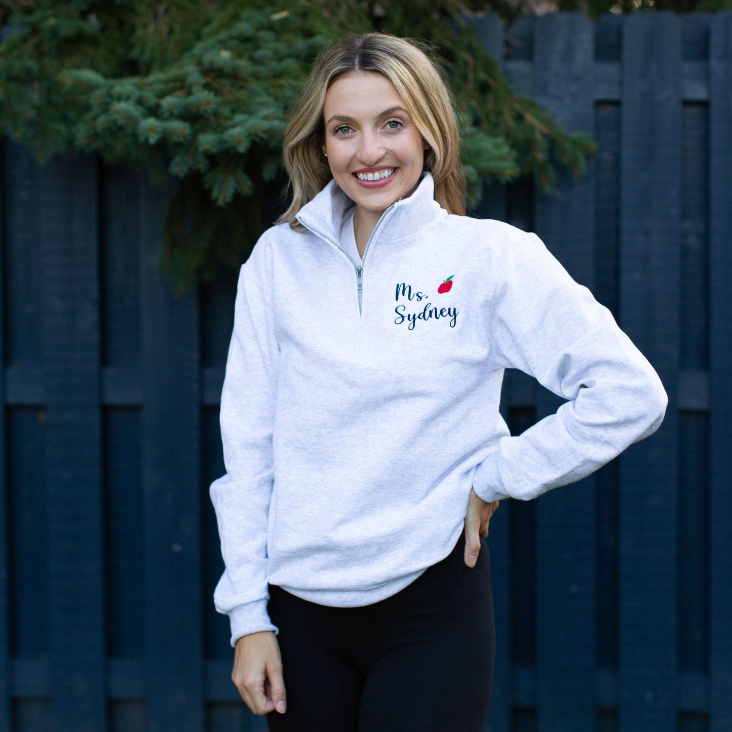 Woman wearing a personalized embroidered light gray quarter zip with mini red apple
