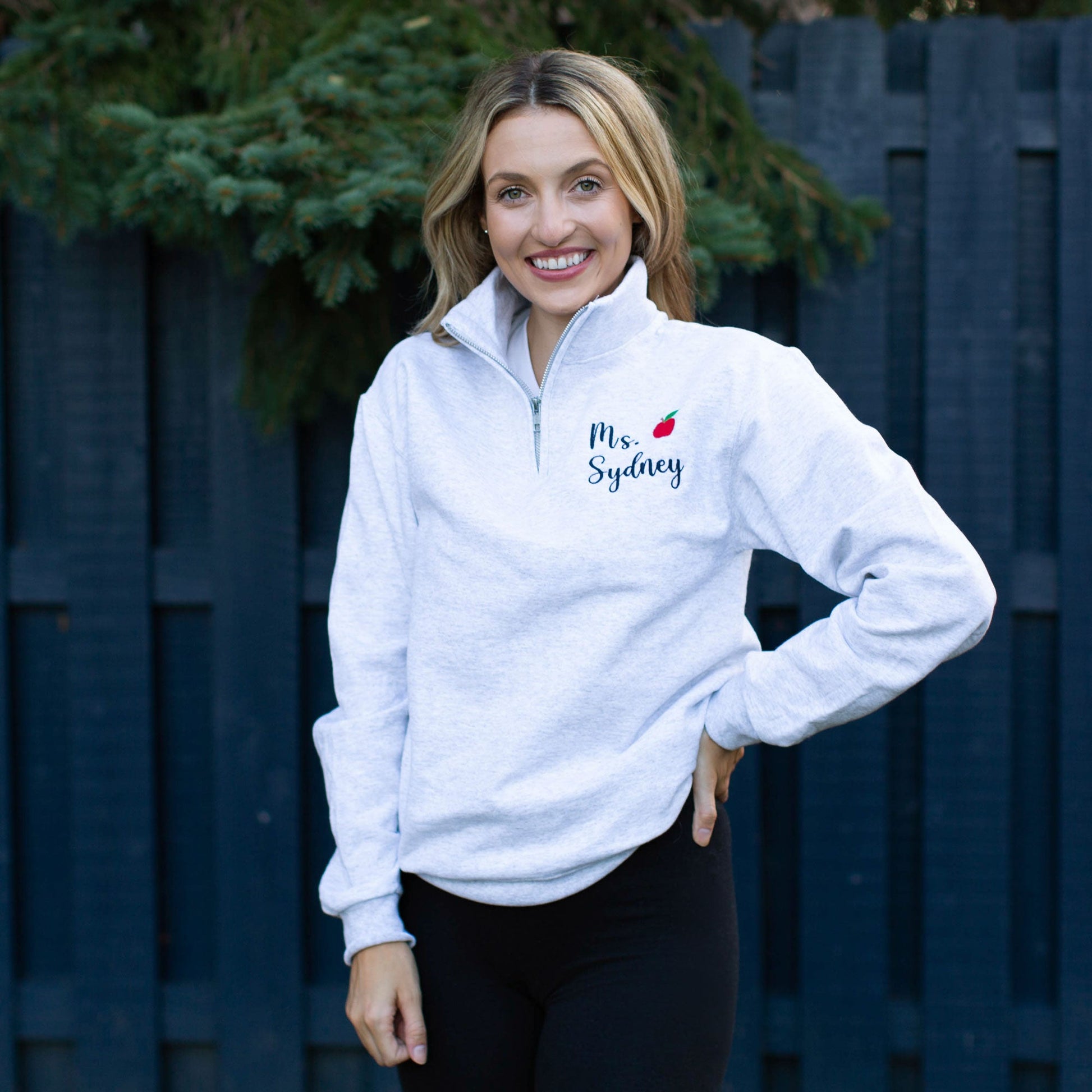 Woman wearing a personalized embroidered light gray quarter zip with mini red apple
