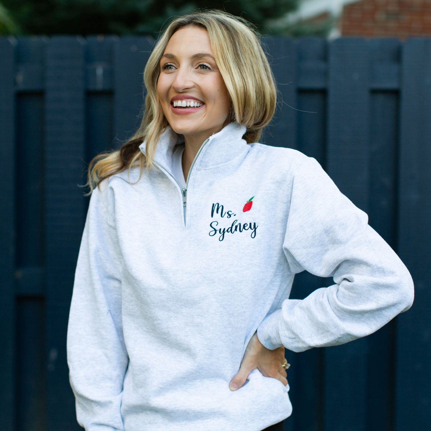 Girl wearing quarter zip pullover sweatshirt with educator's name and small red apple embroidery