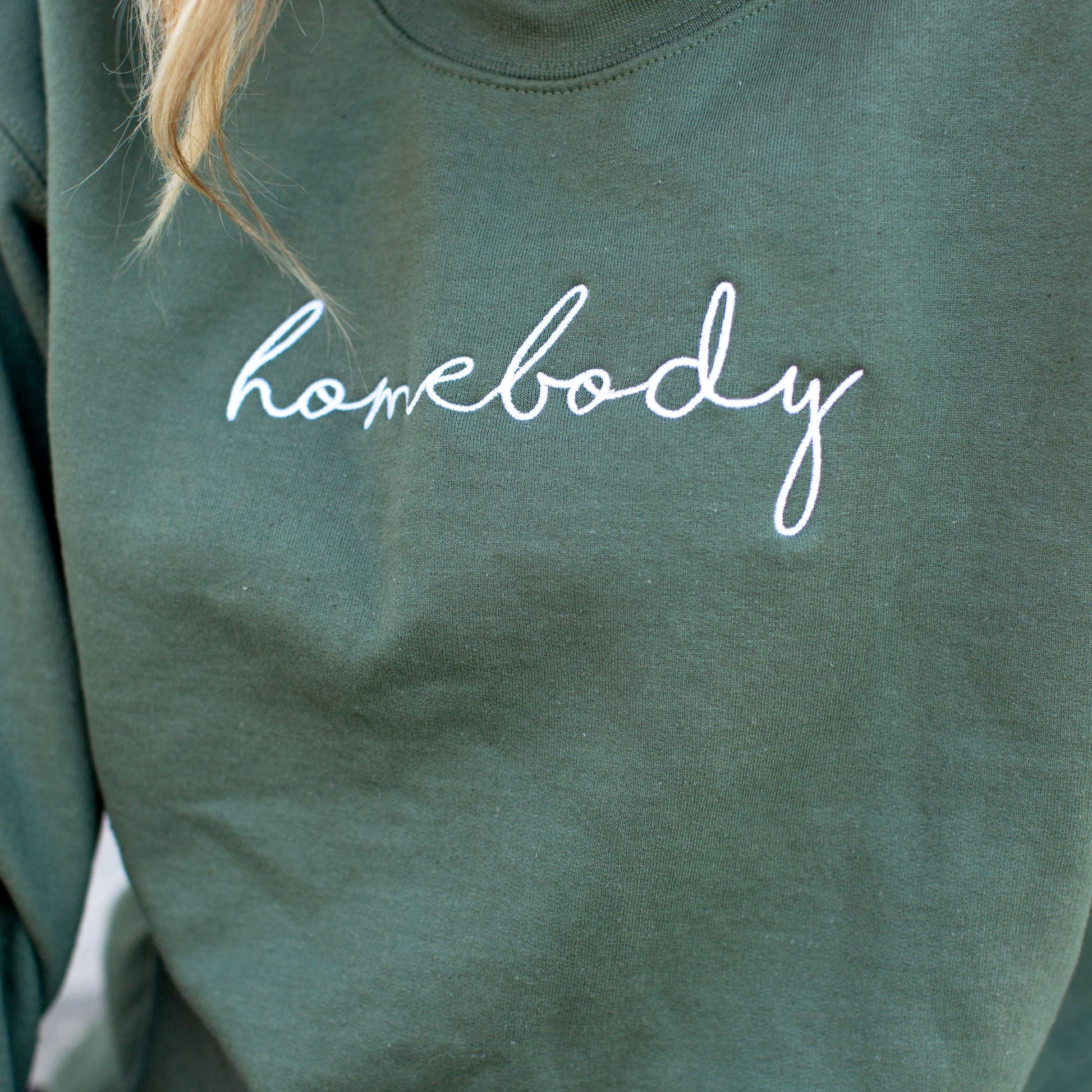 close up of homebody embroidered across the chest on a green crewneck sweatshirt