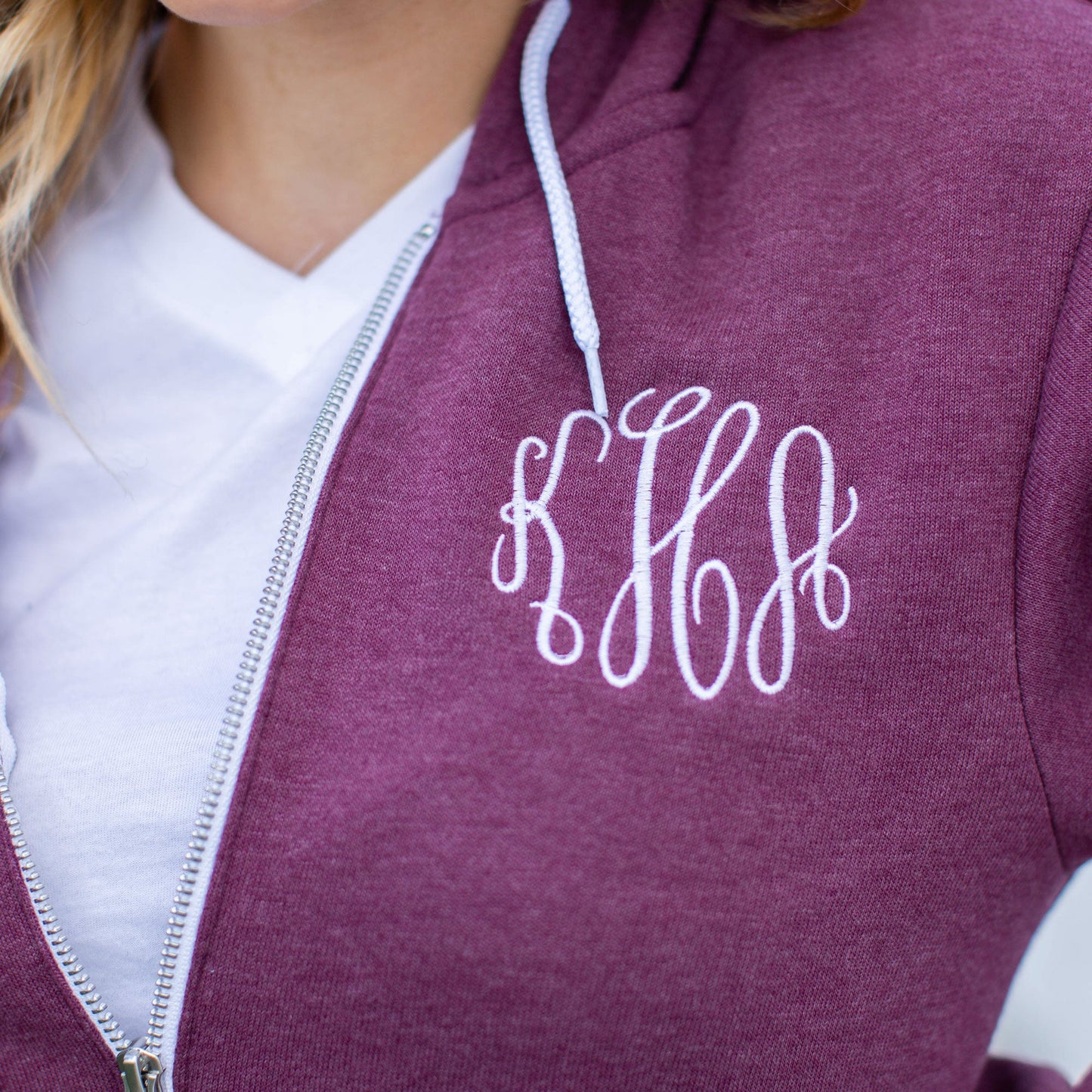 Close up of embroidered three letter script monogram on a heather maroon sweatshirt full zip jacket