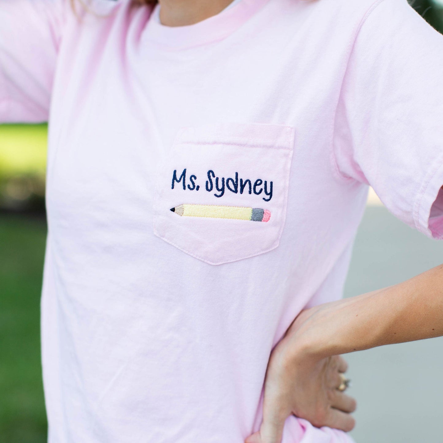 Close up of embroidered Blossom pocket tee educator's name and pencil on pocket