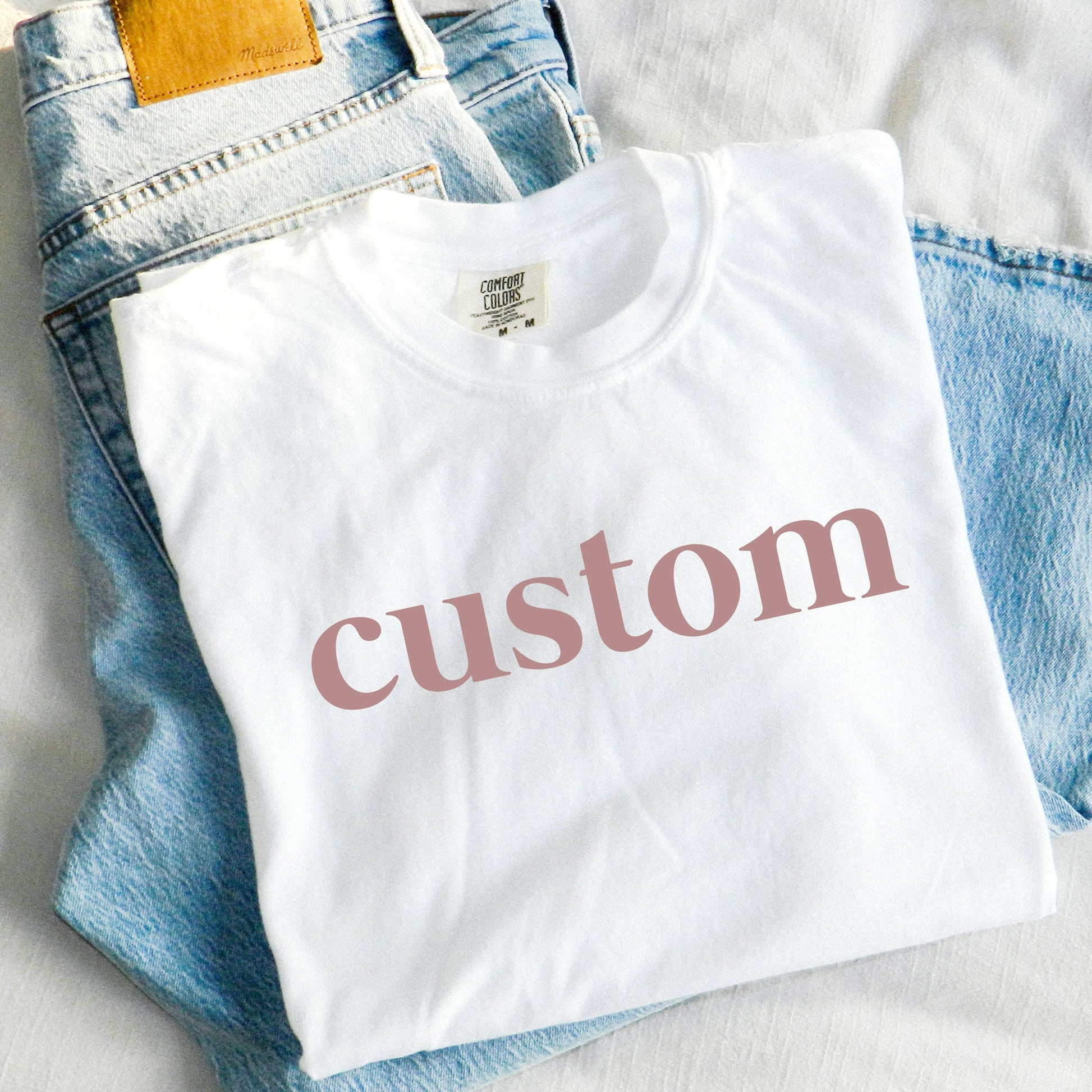 white comfort colors t-shirt with a custom dtg print across the chest in a mauve pink ink