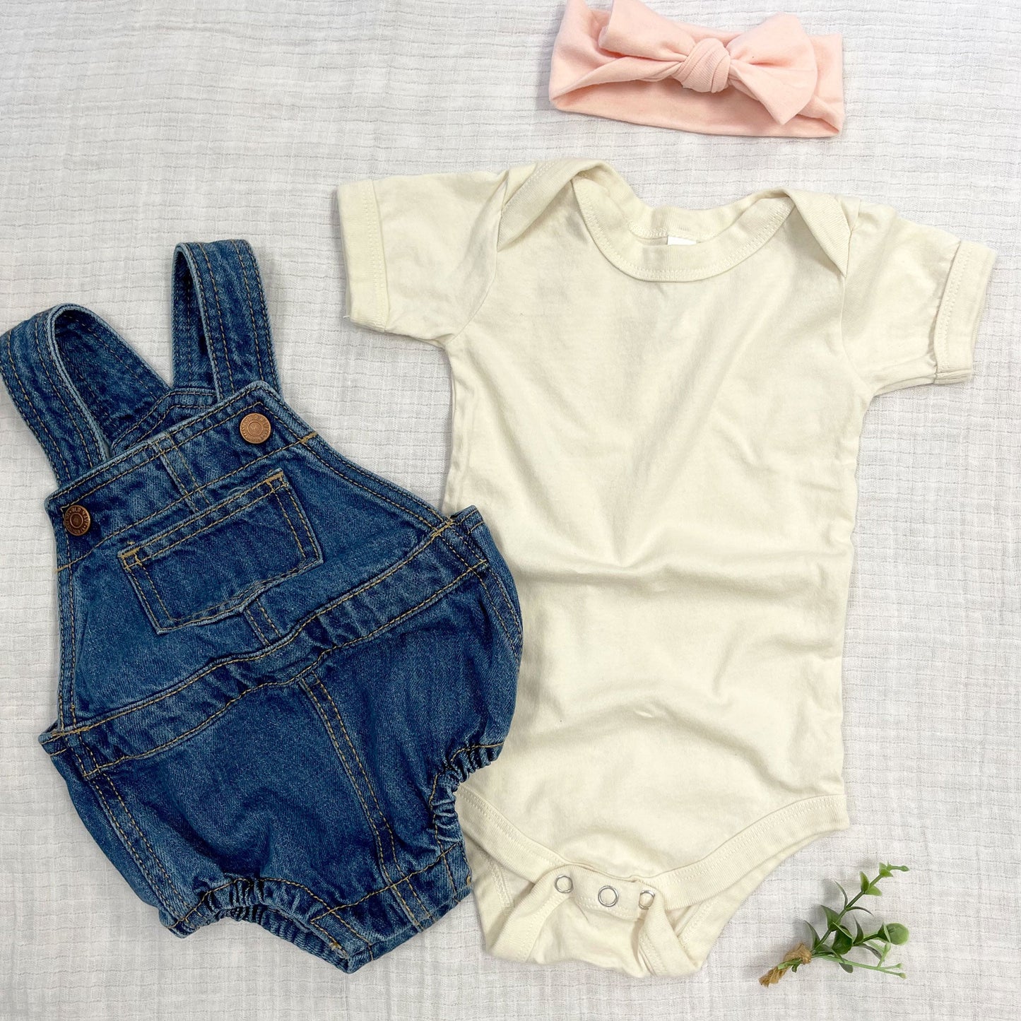 natural short sleeve infant bodysuit flat lay paired with a peach headband and infant denim overalls