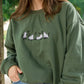 close up of a military green crewneck sweatshirt with embroidered 4 ghost cats embroidered design