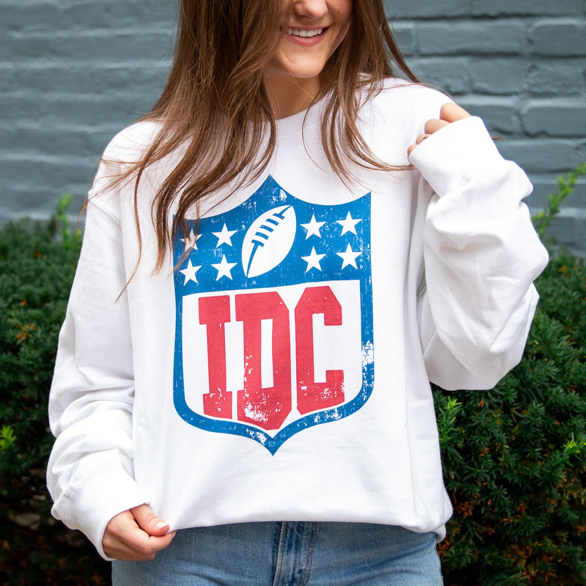 woman wearing oversized white crewneck sweatshirt with an idc printed logo on the front