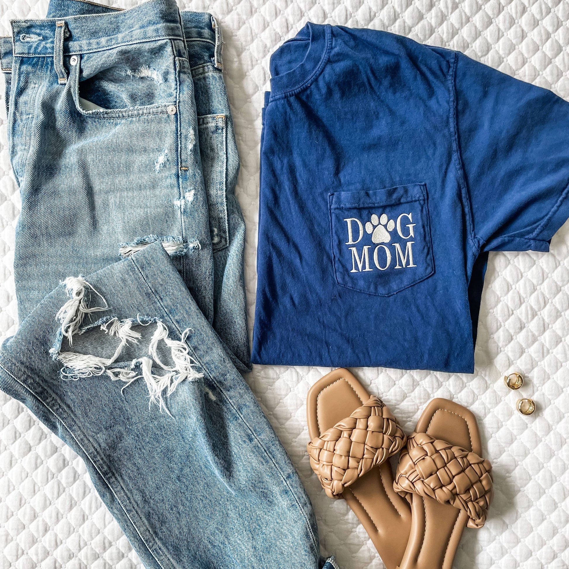 flatlay of outfit featuring distressed jeans, sandals, and navy blue comfort colors tee with dog mom embroidered on the pocket