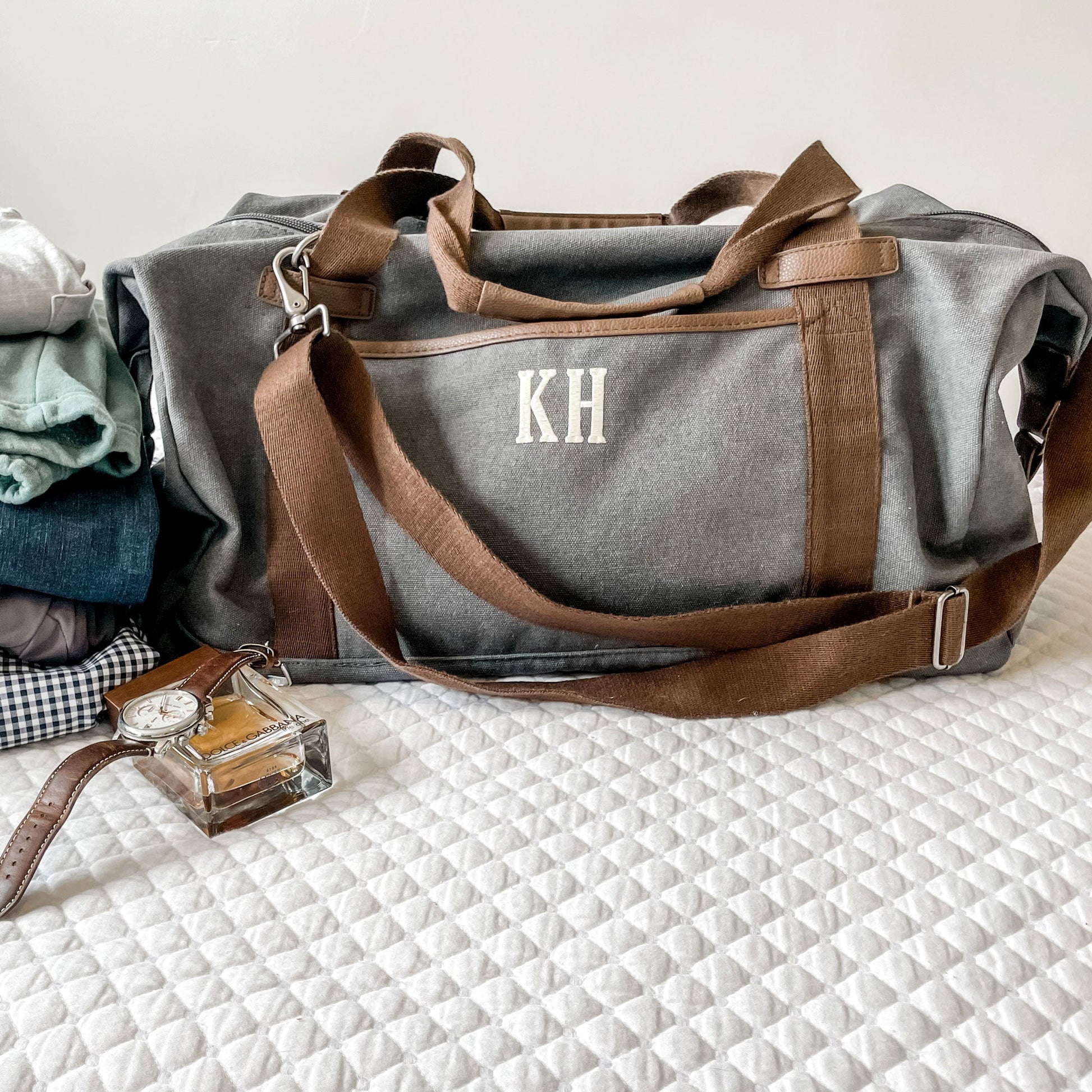 photo of gray duffel with clothing, watch and cologne beside it