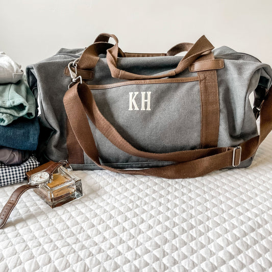 photo of gray duffel with clothing, watch and cologne beside it