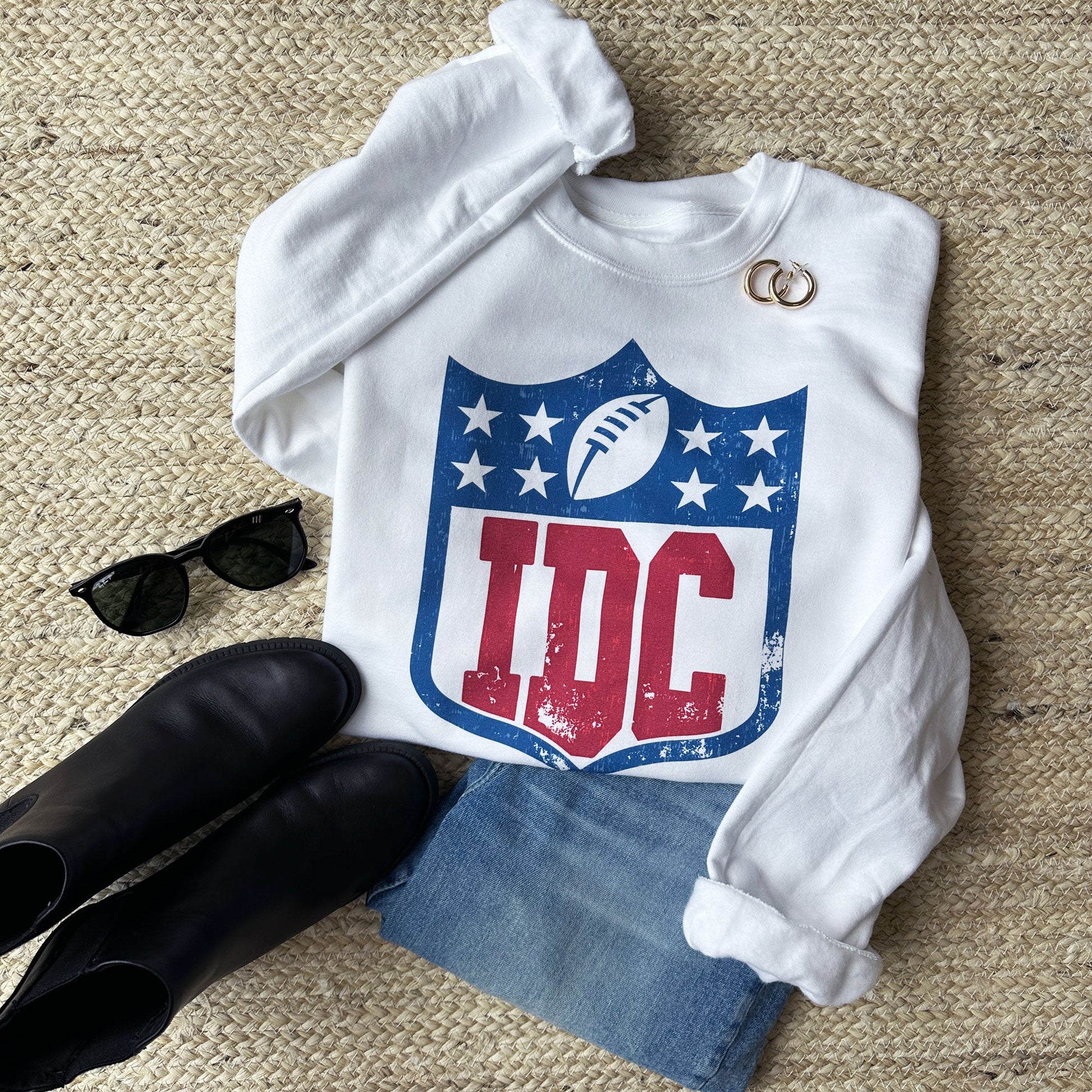 outfit layout featuring jeans, black booties, sunglasses, earrings, and a white pullover crew with an IDC football logo