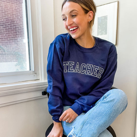 girl wearing blue pullover sweatshirt with teacher embroidered in a vintage block font