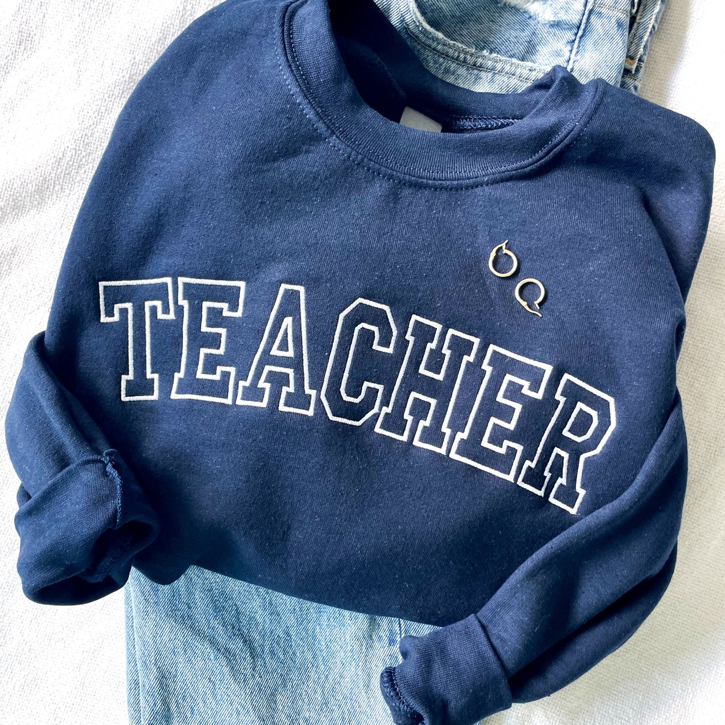 close up of a sweatshirt with teacher embroidered in white thread and a block font on a navy sweatshirt