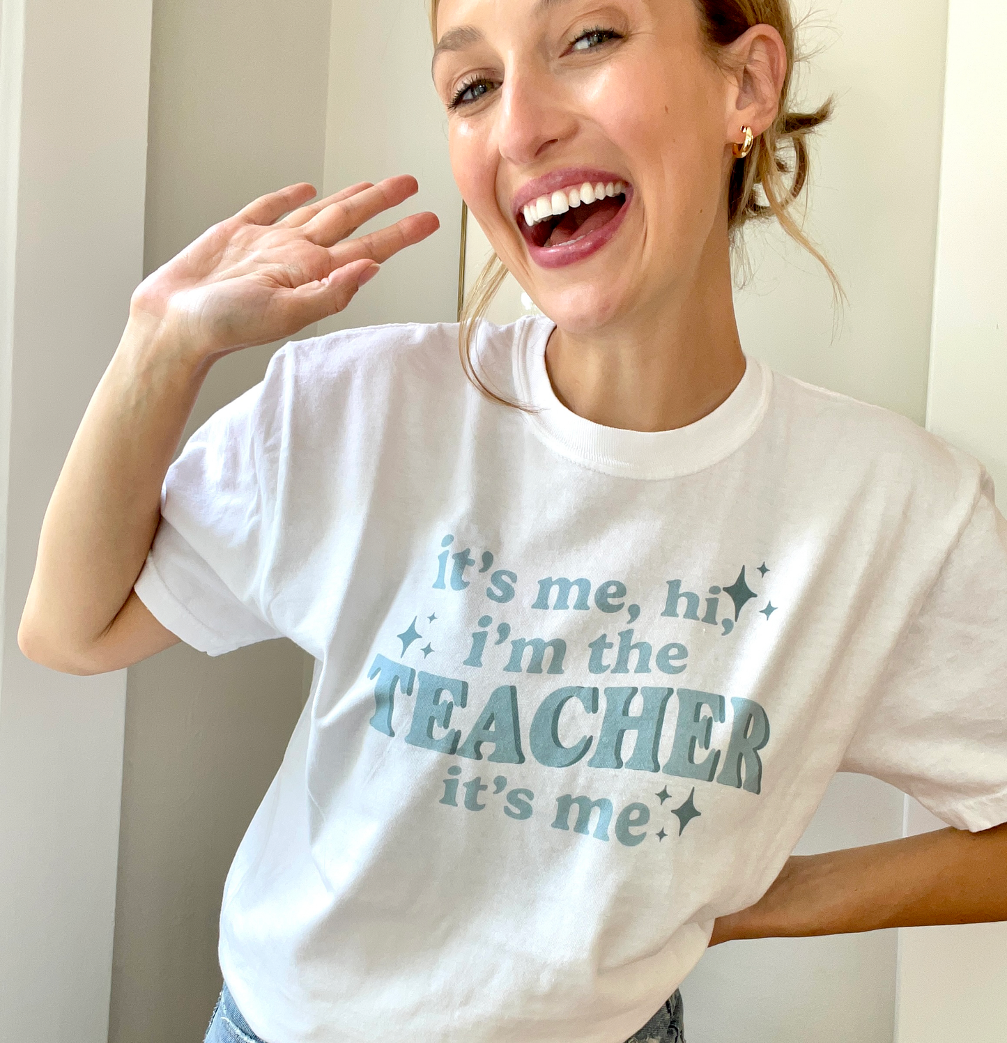 young woman wearing a white t-shirt with a trendy taylor swift inspired design reading 'it's me, hi, i'm th eteacher it's me.'