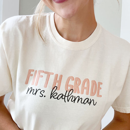 woman wearing an ivory comfort colors t-shirt with a custom grade level and name printed design across the chest