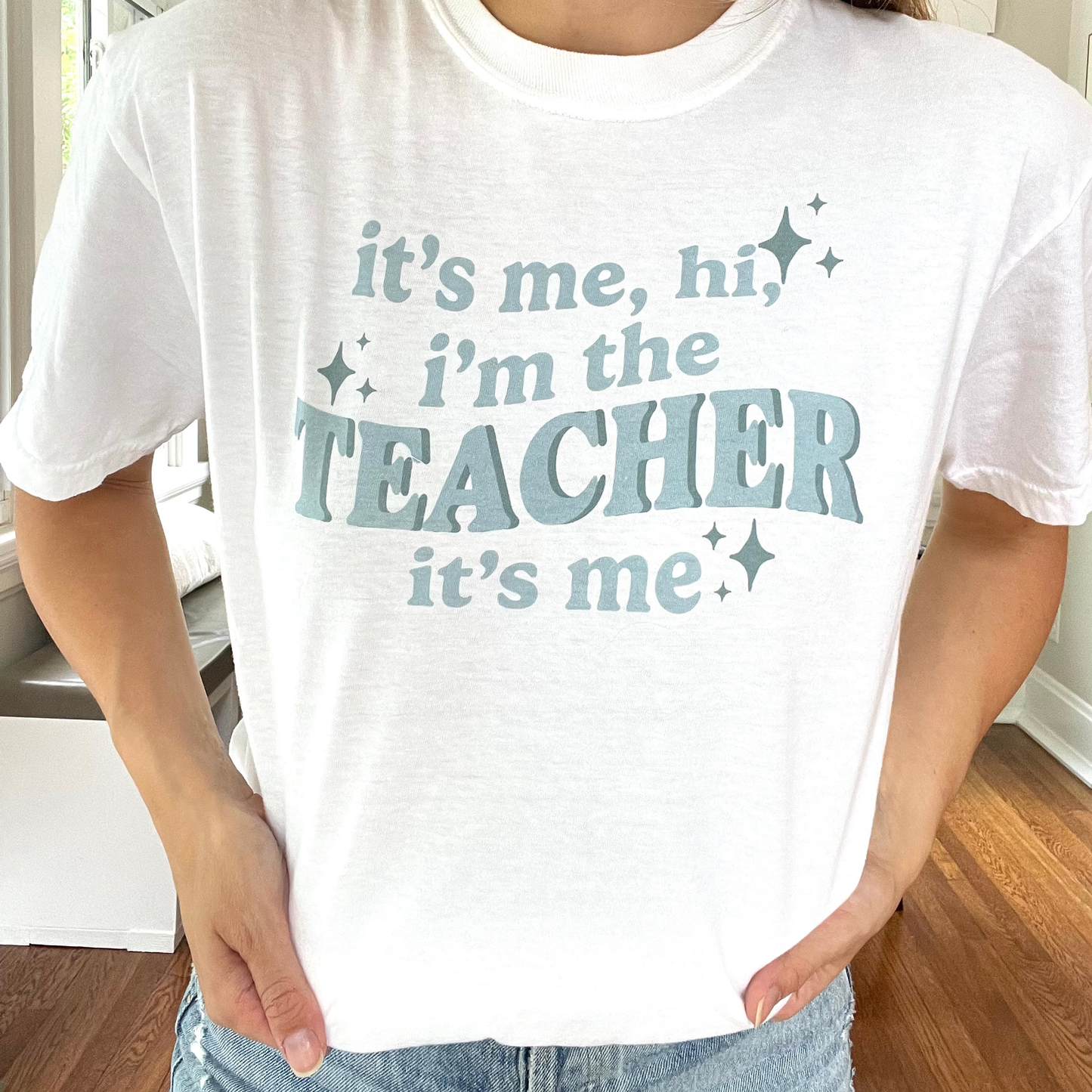 close up of a white comfort colors t-shirt with a custom "it's me, hi, i'm the teacher it's me" DTG printed deisgn across the front