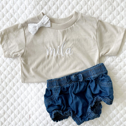 flat lay of tan tee shirt with name embroidered in center