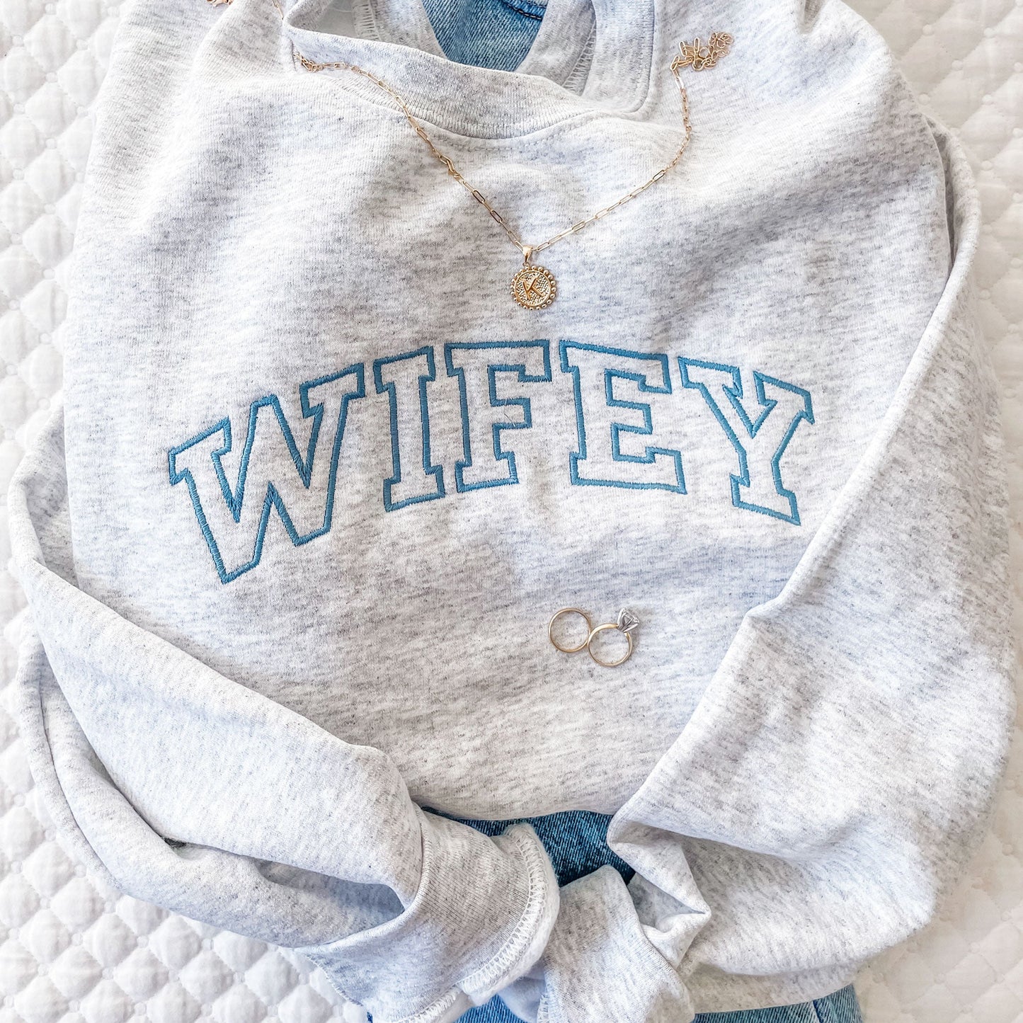 flat lay of sweatshirt with custom athletic block font embroidery across the chest paired with jeans and jewelry.
