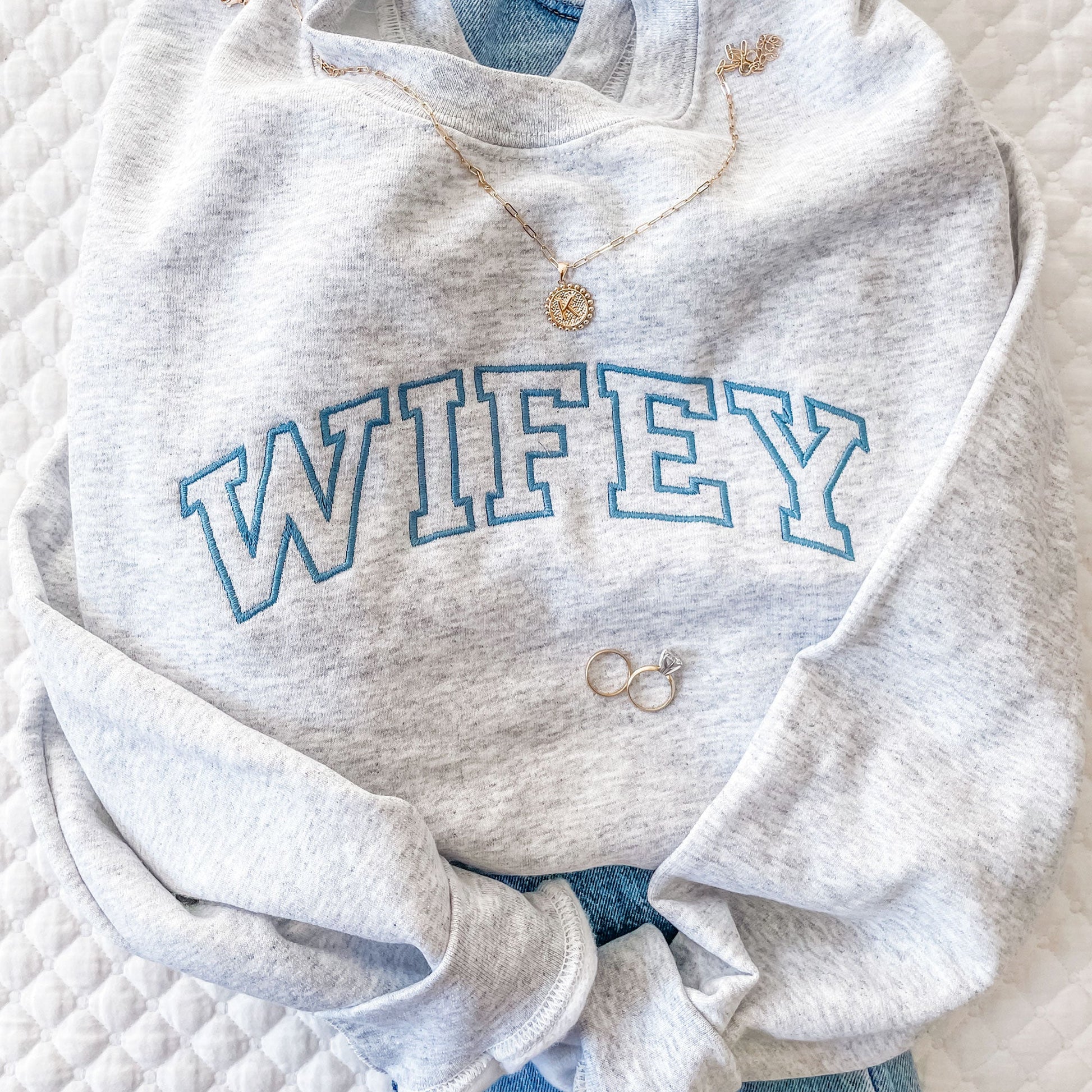 flat lay of sweatshirt with custom athletic block font embroidery across the chest paired with jeans and jewelry.