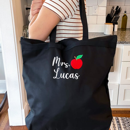 Woman carrying black bag with educator's name and mini apple embroidered on the front