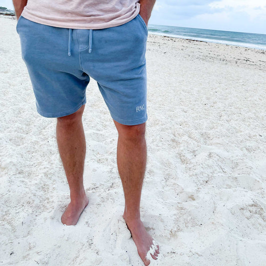 man standing on the beach and wearing a pair of casual sweat shorts with a custom two-letter monogram embroidered near the lower hem of the left leg