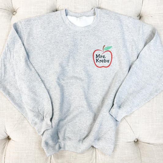Ash gray sweatshirt flaylay with red apple outline and teacher name embroidery 