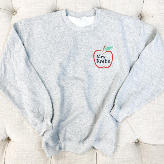 Ash gray sweatshirt flaylay with red apple outline and teacher name embroidery