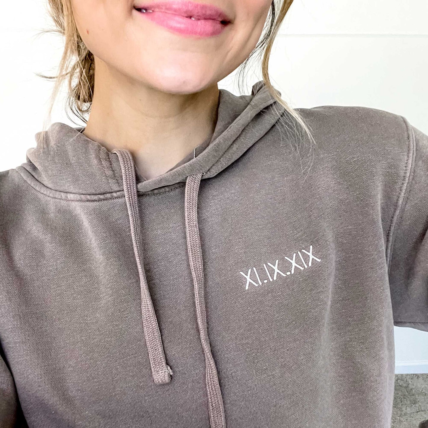 woman wearing a brown hoodie with a custom roman numeral embroidered design on the left chest