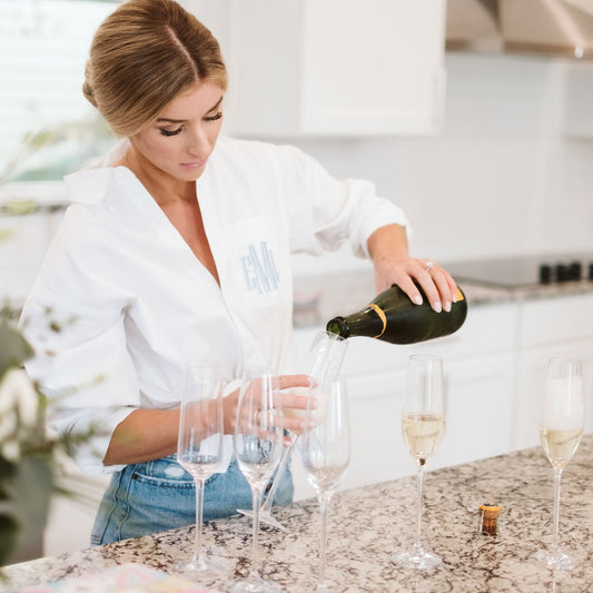 bride pouring a glass of champagne wearing a white dress shirt with personalized embroidery in light blue thread on the pocket