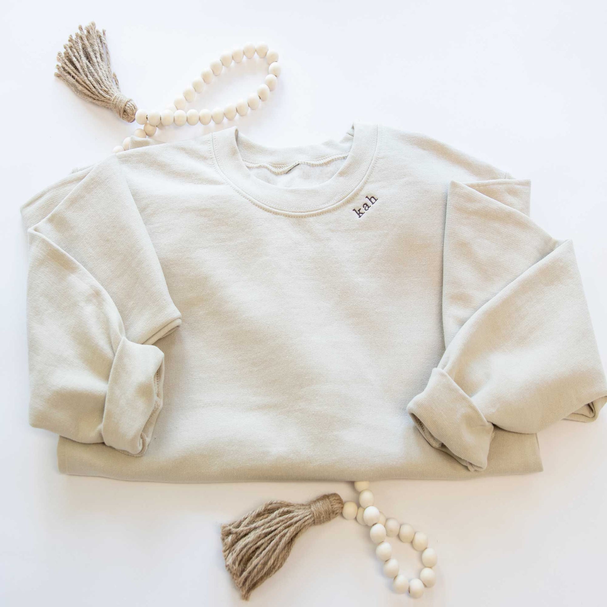 a sand crewneck sweatshirt with embroidered mini initials in all lowercase kah on the neckline in java thread
